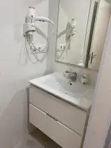 Mueble de lavabo blanco con cajones bajo la encimera, con el espejo y el secador del baño detrás